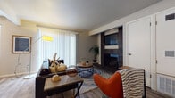 This single-floor residence offers a well-organized layout with distinct living, dining, sleeping, and utility spaces. The living room serves as the centerpiece of the home, highlighted by a striking dark brick fireplace with built-in shelving that anchors the room. Large vertical-blind-covered sliding doors allow generous natural light to fill the space, complementing the wood-look hard flooring. A vibrant accent chair and leather sofa add character to the room's eclectic aesthetic.

The dining area is a dedicated space featuring wood-look flooring, a window with horizontal blinds, and room for a high-top table setup. Adjacent to the dining space, the galley-style kitchen is efficiently designed with white cabinetry, light countertops, wood-look flooring, and stainless steel appliances including a gas range and refrigerator.

The bedroom features plush carpeting, a window for natural light, and ample wall space. The bathroom includes wood-look tile flooring, a tub-shower combination, a white vanity with under-sink cabinetry, and light countertop surfaces, providing a clean and functional layout throughout.