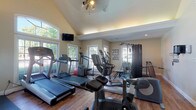 Located at 4311 Camden Cir in Dublin, Ohio, this single-floor private fitness facility is thoughtfully designed to support a comprehensive workout experience. The space features soaring vaulted ceilings with an arched transom window that floods the interior with natural light, complemented by multiple large double-hung windows along the walls offering views of the surrounding greenery. Rich hardwood flooring runs throughout, providing a warm and polished aesthetic that distinguishes this space from a typical gym.

The cardio zone is well-appointed with multiple treadmills, including Life Fitness models, an elliptical trainer, and a stationary bike, all positioned to take advantage of the natural light and outdoor views. A wall-mounted flat-screen television adds entertainment convenience for cardio sessions.

A dedicated strength training area houses a multi-station cable machine, a full dumbbell rack ranging across various weights, adjustable benches, a squat/barbell station, and protective rubber floor mats. A large wall mirror in the weight area enhances spatial perception and supports proper form during lifts.

Additional amenities include a wall-mounted sanitizer dispenser, organized equipment hooks, recessed lighting, and French door access that connects sections of the space seamlessly. The overall ambiance is bright, clean, and purposefully organized, making this a fully equipped private training environment.