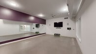 Located at 900 Luxor Ln in Norristown, PA, this dedicated fitness studio at Breathe offers a thoughtfully designed single-floor space built for group classes and individual training alike. The open floor plan provides generous room for movement, finished with durable, easy-to-clean flooring suited for a wide range of exercise activities.

A defining feature of the studio is the expansive wall-to-wall mirror installation, accented by a bold deep-purple accent wall that lends the space a modern, energetic atmosphere. The white walls and recessed ceiling lighting keep the environment bright and functional, while a ceiling fan ensures comfortable airflow during workouts.

A wall-mounted flat-screen television is prominently positioned for instructor-led video workouts or class programming, complemented by integrated wall-mounted speakers for an immersive audio experience. The studio is equipped with a variety of fitness equipment, including dumbbells, kettlebells, resistance tools, a stability ball, step platforms, and exercise mats, making it versatile for multiple training modalities.

Exposed ductwork and industrial-style ventilation add a contemporary edge to the design. Interior frosted-glass windows connect the studio to an adjacent space, allowing light to pass through while maintaining privacy. A private entry door provides convenient access. This studio is a fully functional, professionally outfitted space designed to support an active and dynamic fitness environment.