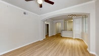 This well-appointed 2-bedroom, 2-bathroom residence in Dallas, TX offers a thoughtfully designed single-floor layout with a comfortable sense of space throughout. The interior is characterized by elegant arched doorways that connect the main living areas, crown molding, and light-toned hardwood-style flooring that flows through the main areas. The open-concept living room features vaulted ceilings with a ceiling fan, large windows that invite natural light, and direct access to an entry door, creating a bright and airy atmosphere. The kitchen is equipped with white shaker cabinetry, granite countertops, stainless steel appliances including a refrigerator, microwave, electric range, and dishwasher, alongside a peninsula with a sink that overlooks the living area. A built-in shelving unit adds a stylish, functional touch near the kitchen. The spacious primary bedroom features plush carpeting, a ceiling fan, and generous natural light from a wide window. The second bedroom is equally comfortable with carpet flooring and a ceiling fan. Both bathrooms are finished with tiled tub-shower combos, granite-topped vanities, and white cabinetry, maintaining a clean, cohesive aesthetic throughout the home.