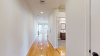 This single-floor unit offers a clean, modern design highlighted by gleaming hardwood floors that run throughout the entire space. A long, well-lit hallway connects all areas of the unit, providing a seamless flow from room to room. The open-concept kitchen serves as the heart of the home, featuring a large center island with dark granite countertops, white shaker cabinetry, a subway tile backsplash, stainless steel appliances, and stylish pendant lighting. Multiple windows flood the kitchen and adjacent living area with natural light. An in-unit stacked washer and dryer is conveniently located just off the kitchen. The bedrooms are generously proportioned, each fitted with large double-hung windows that invite abundant daylight and offer outdoor views. One bedroom includes a dedicated walk-in closet. Two full bathrooms are finished with grey tile flooring, dark wood vanities with white countertops, and tub-shower combinations with white tile surrounds. Recessed lighting throughout and crisp white walls contribute to the bright, airy ambiance of the space, making it feel open and welcoming at every turn.