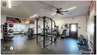 Located at 2190 Ocean Reef Pl in Raleigh, NC, this fitness center spans a single floor and is divided into two exercise rooms, together offering a comprehensive workout environment. The space features durable rubber flooring throughout, providing both safety and comfort during training sessions.

The primary exercise room is appointed with a variety of strength and cardio equipment, including a power rack with weight plates, treadmills, ellipticals, a stair climber, and cable machines. A striking sports-themed mural covers one wall, incorporating bold red and black imagery that energizes the atmosphere. Linear LED lighting runs along the ceiling, complemented by ceiling fans that help maintain air circulation. Large mirrors along the walls enhance the sense of openness and allow users to monitor their form.

The secondary exercise room continues the fitness theme with additional cardio machines, including an Echelon bike and treadmills, along with a full free weight station featuring a dumbbell rack, kettlebells, and a flat bench. Natural light filters in through multiple windows, brightening the space. Glass doors connect the two rooms and provide a view into an adjacent recreation area. The overall aesthetic is clean, modern, and motivational, making this fitness center a fully functional resource for residents.