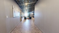 Located on Chapel Street South in Hartford, CT, this thoughtfully designed amenity space spans a generous single floor, offering a diverse range of functional zones tailored for both relaxation and productivity. A defining architectural feature throughout is the bold, three-dimensional geometric ceiling treatment in a dark metallic finish, which lends a sophisticated, upscale character to every area.

The expansive main lounge serves as the heart of the space, furnished with plush velvet seating, vibrant area rugs, and curated artwork adorning the walls. A stone-accented fireplace wall with a mounted flat-screen TV creates an inviting focal point. Adjacent to the lounge, a lively game room features a full-size pool table, bar-height seating, and wall sconce lighting, ideal for social gatherings.

A well-appointed conference area offers a large shared work table with comfortable rolling chairs, glass-partitioned walls providing views into the fitness center, and colorful artwork that energizes the workspace. The fitness center itself is visible through floor-to-ceiling glass doors, equipped with cardio machines and exercise equipment against a vibrant orange accent wall.

A cozy private meeting room, accented with a richly textured wood-panel feature wall, provides an intimate setting for small gatherings. Light wood-look flooring and tile throughout tie the various zones together seamlessly, creating a cohesive and dynamic environment.