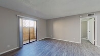 This single-floor unit offers a thoughtfully designed layout that maximizes its comfortable footprint. The open-concept living room and kitchen area serve as the heart of the home, with durable wood-look vinyl plank flooring flowing throughout. The living room is bathed in natural light, courtesy of a sliding glass door that leads to a private outdoor patio enclosed by a latticed wooden fence — a charming retreat. The front entry opens directly into this living space, which features neutral gray walls and crisp white baseboards that lend a clean, modern aesthetic.

The kitchen is efficiently arranged in a galley-style layout, featuring white shaker cabinets with contrasting black hardware, white countertops, and a peninsula that provides additional prep space. Black appliances, including a refrigerator and dishwasher, add a bold accent to the bright cabinetry.

The generously sized primary bedroom is carpeted for comfort and includes two windows that allow ample natural light to fill the room. A ceiling fan with a built-in light fixture adds both function and airflow. The bedroom connects to a dedicated walk-in closet, carpeted and equipped with a built-in hanging rod, offering substantial storage. Textured ceilings are present throughout, adding a classic residential character to the space.