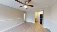This single-floor unit offers a clean, functional layout with a warm and neutral aesthetic throughout. The living area is highlighted by light hardwood-style flooring, crown molding, and a ceiling fan with integrated lighting, creating a comfortable and airy atmosphere. A chair rail detail runs along the walls, adding a subtle architectural touch. A window allows natural light to fill the space, further enhancing its open feel.

The galley-style kitchen is efficiently designed, featuring gray shaker cabinets with brushed hardware, a light marble-look countertop, a stainless steel sink, and black appliances including a refrigerator, electric range, and overhead microwave. The kitchen opens visually toward the living area, maintaining a connected flow.

The bedroom is a calm, well-proportioned space with matching hardwood-style flooring, crown molding, a ceiling fan, and a window that brings in natural light. A six-panel door leads to an attached space, likely a closet or en-suite area, offering added convenience and storage.

The bathroom features a full-size soaking tub with shower, white subway tile surround accented by a decorative mosaic tile border in warm earth tones, and a clean, bright finish. Throughout the unit, consistent flooring, neutral tones, and thoughtful details create a cohesive and inviting living environment.