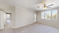 Located at 7401 W Washington Ave in Las Vegas, NV, this single-story home offers four bedrooms, two bathrooms, and a well-designed layout across a generously sized floor plan. The living room and kitchen share an open, connected area, with the kitchen showcasing crisp white shaker cabinets, white subway tile backsplash, light wood-style flooring, and stainless steel appliances including a refrigerator, range, and over-the-range microwave. The bright, neutral-toned bedrooms feature plush carpeting, ceiling fans, and large windows dressed with vertical blinds that invite natural light. The primary bedroom is notably spacious, finished with elegant crown molding and direct access to an adjoining area. The bathrooms are clean and functional, with one featuring a tub-shower combination enclosed by sliding glass doors and a frosted glass block window above for added privacy and light. Three closets provide ample storage, including a walk-in closet with wire shelving and light wood-style flooring. A dedicated laundry room houses a full-size side-by-side washer and dryer. Throughout the home, a consistent neutral color palette, crown molding details, and ceiling fans contribute to a comfortable and cohesive living environment.