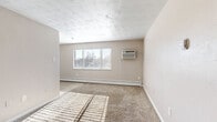 Located at 1515 Seventh Ave in Greeley, Colorado, this efficiently designed single-floor unit offers a practical and functional layout. The living room serves as the heart of the space, featuring soft wall-to-wall carpeting, neutral beige walls, and a textured ceiling that adds subtle character. A window fitted with blinds allows natural light to pour in, casting bright patterns across the floor, while a wall-mounted air conditioning unit and baseboard heating ensure year-round comfort.

The kitchen is positioned adjacent to the living area and is equipped with white cabinetry, a tile backsplash, and a stainless steel refrigerator. An in-unit washer is conveniently located within the kitchen area, adding practical value. Hardwood-style flooring transitions seamlessly from the kitchen into the connecting hallways.

The bathroom is clean and well-appointed, featuring a tiled tub-shower combination, a toilet, and a vanity with a light-colored countertop and mirror. White tile surrounds the tub area, maintaining a bright, crisp aesthetic.

Three closets distributed throughout the unit provide generous storage relative to the overall footprint. Two hallways connect the various rooms, creating a logical and easy-to-navigate flow throughout the space.