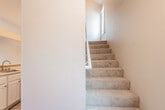 This well-designed two-story residence offers a thoughtful layout that balances open communal spaces with comfortable private areas. The main level features an open-concept living and kitchen area with warm hardwood-style flooring throughout. The kitchen is equipped with white cabinetry, light countertops, stainless steel appliances including a refrigerator and gas range, and a convenient breakfast bar that connects seamlessly to the living space. A secondary sink area is also found on the main level near the staircase. Carpeted stairs lead to the upper floor, where the vaulted ceilings create an impressive sense of height and volume. The upper level includes a spacious primary bedroom with vaulted ceiling details and direct access to a full bathroom featuring a tub-shower combo, single vanity, and a small window for natural light. Additional bedrooms on this floor feature hardwood-style flooring, generous natural light from well-placed windows with vertical blinds, and ample wall space. A standout feature is the room with soaring vaulted ceilings and sliding glass doors opening to a private balcony with outdoor views. Throughout the residence, neutral warm-toned walls and consistent flooring create a cohesive and inviting atmosphere.
