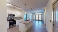 This single-story residence is designed with an open-concept layout that seamlessly connects the kitchen and living area, creating a bright and functional living space. The kitchen is well-appointed with white shaker-style cabinetry, granite countertops, and stainless steel appliances, including a range, microwave, and refrigerator. A central island with a double undermount sink and pendant lighting serves as both a prep area and a natural divider between the kitchen and living space. Track lighting above the kitchen provides additional illumination. The living area extends toward a set of glass French doors that open to a private balcony, where a ceiling fan adds comfort. Natural light flows generously throughout this open space.

The bedrooms feature plush carpeting, ceiling fans, and windows with blinds. Each bedroom is complemented by a spacious walk-in closet outfitted with wire shelving systems for organized storage. The two bathrooms mirror the home's refined aesthetic, showcasing granite-topped white vanities, tile flooring, and framed mirrors with contemporary lighting. One bathroom includes a soaking tub with tiled surround. Wood-look flooring runs throughout the main living areas, tying the design together cohesively.