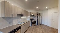 This single-floor unit offers a thoughtfully designed layout that balances modern style with everyday functionality. The kitchen serves as a standout feature, showcasing light wood-grain cabinetry extending to the ceiling, a classic subway tile backsplash, and a full suite of stainless steel appliances including a gas range, over-the-range microwave, refrigerator, and dishwasher. A built-in wine rack adds a refined touch, while recessed lighting and durable wood-look flooring complete the contemporary aesthetic. The open design of the kitchen allows for a seamless flow into the adjacent living area, which is bathed in natural light and features the same resilient flooring underfoot. The bedroom is carpeted for comfort and includes a ceiling fan with integrated lighting, as well as a window that invites natural light and exterior views, creating a bright and airy atmosphere. The bathroom is finished in a clean, minimalist style with white tile surrounding a full soaking tub and shower combo, complemented by wood-look flooring and a vanity with stone-style countertops. In-unit laundry is also present, adding to the overall convenience of this well-designed space.