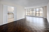Located on the 18th floor at 450 Walmer Rd in Toronto's prestigious Forest Hill neighbourhood, this well-appointed 3-bedroom, 2-bathroom unit offers a functional and comfortable layout across a single floor. The open living room is a standout feature, characterized by expansive floor-to-ceiling windows that flood the space with natural light and frame sweeping city views. Classic parquet hardwood flooring runs throughout the main living areas and bedrooms, adding warmth and character to the neutral, light-toned interiors. The galley-style kitchen is neatly outfitted with white cabinetry, granite-style countertops, a subway tile backsplash, tile flooring, and a stainless steel refrigerator, opening conveniently toward the living area. The generously sized primary bedroom features a large window with city views and sliding panel closet doors, while the additional bedrooms are well-proportioned with parquet flooring. The two bathrooms include one with a full soaking tub and white tile surround, and a second with a mirrored medicine cabinet, extended vanity, and distinctive mosaic tile flooring. Two hallways provide practical circulation throughout the unit, completing this well-structured urban residence.