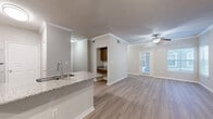 This thoughtfully designed single-story residence offers a comfortable and functional layout across its 1 bedroom and 1 bathroom. The open-concept living and kitchen area forms the heart of the home, featuring light hardwood-style flooring, crown molding, and a ceiling fan that enhances airflow throughout the space. Large windows and a glass-panel exterior door flood the living room with natural light, creating a bright and welcoming atmosphere.

The kitchen is a standout feature, anchored by a peninsula with elegant granite countertops that double as a breakfast bar. Warm-toned wood cabinetry, stainless steel appliances — including a range, microwave, and refrigerator — and a deep undermount sink complete this well-equipped cooking space. A mirrored accent wall adjacent to the kitchen adds depth and reflects light throughout the open area.

The bedroom is a spacious and tranquil retreat, finished with plush wall-to-wall carpeting, a vaulted ceiling with a ceiling fan, and a generous window that invites natural light and outdoor views. A dedicated closet provides ample storage. The bathroom is clean and functional, featuring a full tub-shower combination with white tile surround and wood-style flooring. A separate closet rounds out the practical storage options in this well-balanced residence.