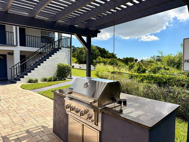 Encantadora zona al aire libre con una elegante parrilla de acero inoxidable bajo una pérgola con estilo, rodeada de exuberante vegetación y un acogedor patio. - Waterside Village