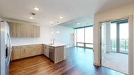 This contemporary single-floor residence blends modern design with functional living across a well-appointed open layout. Rich hardwood flooring runs throughout the main living areas, complemented by crisp white walls and exposed concrete ceilings that lend an urban, industrial character to the space.

The kitchen is a standout feature, equipped with light wood cabinetry, a sleek white quartz peninsula with an undermount sink, stainless steel appliances including a refrigerator, range, microwave, and dishwasher, and a classic subway tile backsplash. Pendant lighting above the peninsula and recessed ceiling lights provide layered illumination. The kitchen flows seamlessly into the open living area, which is bathed in natural light through expansive floor-to-ceiling windows offering broad outdoor views.

The bedrooms are carpeted for comfort and feature exposed concrete ceilings. Several bedrooms include direct access to private balconies through full-height sliding glass doors, framing open panoramic views of the surrounding landscape. One bedroom includes a walk-in closet with built-in shelving. A ceiling fan adds to the comfort of the primary bedroom suite.

The bathrooms are finished with marble-style porcelain tile on both floors and walls. One bathroom features a soaking tub with tiled surround and a floor-to-ceiling window, while another offers a glass-enclosed walk-in shower. The entry hallway is wide and welcoming, with a recessed panel and closet access completing the practical layout.