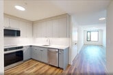 Located at 873 Communipaw Avenue in Jersey City, NJ, this modern 2-bedroom, 2-bathroom residence offers a thoughtfully designed single-floor layout with a clean, contemporary aesthetic throughout. Warm hardwood flooring flows seamlessly across every room, complemented by crisp white walls and recessed lighting that create a bright, welcoming atmosphere.

The open hallway connects all areas of the home efficiently, with the kitchen positioned off the entry corridor. The kitchen is outfitted with sleek gray flat-front cabinetry — both upper and lower — white quartz countertops, a vertically stacked tile backsplash, and stainless steel appliances, including a full-size refrigerator.

The living room offers generous proportions with recessed lighting and direct sightlines down the hallway, giving the space an open, airy feel. Both bedrooms are well-sized, with the primary bedroom providing ample room and a double-door closet. Each bedroom features large black-framed windows that flood the rooms with natural light and offer views of the surrounding Jersey City neighborhood. The second bedroom includes a wall-mounted HVAC unit for individualized climate control.

The two bathrooms are finished with clean, modern tile work. One features a sliding glass-door walk-in shower with mosaic tile flooring, while the other includes a full soaking tub with large-format wall tile. Three closets and an in-unit laundry room complete this well-appointed home.