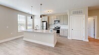 Located in Charleston, SC, this well-appointed 4-bedroom, 2-bathroom single-story home offers a thoughtfully designed open-concept layout with a clean, contemporary aesthetic. The combined kitchen and living area serves as the heart of the home, anchored by a large center island with a granite countertop and pendant lighting overhead. The kitchen features light wood-tone cabinetry, a stylish tile backsplash, stainless steel appliances, and light wood-style flooring that flows seamlessly throughout the main living spaces. Large windows fitted with blinds invite abundant natural light into the living area, which also includes a ceiling fan and sliding glass door access to the outdoors. The four bedrooms offer comfortable retreats, with plush carpeting, ceiling fans, and generous windows that frame views of the surrounding greenery. The primary bedroom provides a well-sized layout suited for various furniture arrangements. Both bathrooms are finished with wood-tone cabinetry, granite-topped vanities, brushed nickel hardware, and light hardwood-style flooring. The primary bathroom includes a walk-in glass-enclosed shower. Additional storage is provided by two closets, and a hallway connects the private spaces with ease. Neutral warm-toned walls and clean white trim throughout lend the home a bright, move-in-ready feel.