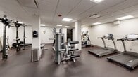 The fitness center at 1225 Santa Fe in Denver, Colorado is a well-appointed, single-floor exercise facility designed to support a comprehensive workout experience. The space features a drop-panel ceiling with recessed fluorescent lighting that keeps the room bright and energizing throughout. Durable rubber flooring covers the entire area, providing both safety and comfort during workouts.

The cardio section is equipped with a treadmill, elliptical machine, and a rowing machine, offering a variety of aerobic training options. For strength training, the facility includes a multi-station cable machine with adjustable pulley systems, a power rack with a pull-up bar, a weight bench, and a dedicated dumbbell rack stocked with a full range of free weights. A TKO heavy punching bag and a wall-mounted speed bag station add a combat fitness element to the space.

A flat exercise mat is available for floor work and stretching, and a stability ball rounds out the functional fitness offerings. Residents can stay hydrated at a wall-mounted dual water fountain station. The clean, neutral white walls and structural support columns give the space a modern, no-frills aesthetic. The layout is thoughtfully organized to allow users to move freely between equipment zones, making this fitness center a practical and fully functional amenity.
