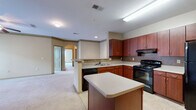 Located at 100 Stonecrest Blvd in Stonecrest, Georgia, this single-floor residence offers a thoughtfully designed layout that balances functionality and comfort throughout. The kitchen serves as a central highlight of the home, featuring rich mahogany-toned cabinetry, a mosaic tile backsplash, light countertops, and a suite of black appliances including a range, dishwasher, and refrigerator. A central kitchen island provides additional prep and counter space, while tile flooring adds durability underfoot. The kitchen flows openly into the adjoining living area, which is finished with plush carpeting and connected via an elegant arched passageway, adding architectural character to the space. Bedrooms are generously proportioned with soft carpet, large windows that invite natural light and outdoor views, and access to walk-in closets with built-in shelving. The bathroom is well-appointed with a rich wood vanity, light countertops, a large mirror, tile flooring, and a tub-shower combination with decorative tile accents. A dedicated in-unit laundry room with a full-size washer and dryer adds everyday convenience. Overall, the space presents a clean, neutral palette with warm wood tones, creating a welcoming and practical living environment.