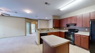 Located at 100 Stonecrest Blvd in Stonecrest, Georgia, this single-floor residence offers a thoughtfully designed layout that balances functionality and comfort throughout. The kitchen serves as a central highlight of the home, featuring rich mahogany-toned cabinetry, a mosaic tile backsplash, light countertops, and a suite of black appliances including a range, dishwasher, and refrigerator. A central kitchen island provides additional prep and counter space, while tile flooring adds durability underfoot. The kitchen flows openly into the adjoining living area, which is finished with plush carpeting and connected via an elegant arched passageway, adding architectural character to the space. Bedrooms are generously proportioned with soft carpet, large windows that invite natural light and outdoor views, and access to walk-in closets with built-in shelving. The bathroom is well-appointed with a rich wood vanity, light countertops, a large mirror, tile flooring, and a tub-shower combination with decorative tile accents. A dedicated in-unit laundry room with a full-size washer and dryer adds everyday convenience. Overall, the space presents a clean, neutral palette with warm wood tones, creating a welcoming and practical living environment.