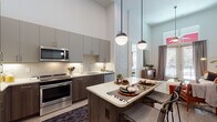This thoughtfully designed single-floor residence makes a striking impression with its soaring ceilings that lend an open, airy ambiance throughout the living spaces. The open-concept kitchen is a standout feature, showcasing two-tone cabinetry in grey and warm wood tones, stainless steel appliances including a range, microwave, dishwasher, and refrigerator, as well as a tile backsplash and under-cabinet lighting. A central island with a quartz countertop and bar seating serves as both a functional workspace and casual dining area, illuminated by a pair of globe pendant lights. Light wood-style flooring flows seamlessly through the kitchen and living areas. The living room offers generous vertical space with walls tall enough to accommodate large-scale artwork, creating an impressive yet comfortable setting. Two bedrooms are present, each featuring large windows that draw in natural light and offer outdoor views. One bedroom includes access to a private walk-in closet with built-in shelving and hanging rods. The residence includes two full bathrooms: one featuring a double vanity with dark wood cabinetry and a tub-shower combination with subway tile surround, and a second bathroom with a walk-in glass-enclosed shower and matching tilework. The overall aesthetic is clean, contemporary, and cohesive throughout.
