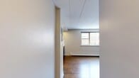 Located in Chicago's Edgewater neighborhood, this efficiently designed single-floor unit at 6119 N Kenmore Ave offers a well-organized layout comprising a living room, kitchen, bathroom, and closet. Rich hardwood flooring flows throughout, lending warmth and continuity to the space. The living room is bright and open, featuring large windows that frame views of the surrounding cityscape and allow natural light to fill the room. A baseboard heating system and wall-mounted AC unit ensure year-round comfort. The kitchen is a standout feature, showcasing dark espresso cabinetry, light quartz countertops, a classic white subway tile backsplash, and stainless steel appliances including a refrigerator, microwave, and cooktop. The bathroom offers a clean, modern finish with a tiled tub surround in an earthy mosaic pattern, a white vanity, and a mirrored medicine cabinet. A dedicated closet provides additional storage. Neutral wall tones and a paneled ceiling complete the clean, functional aesthetic throughout. This unit is a practical and stylish urban space suited for those seeking an efficient Chicago address.