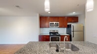 Located at 7022 Gentle Shade Rd in Columbia, Maryland, this single-floor residence offers a well-designed layout with thoughtfully appointed finishes throughout. The kitchen serves as a central highlight, showcasing rich cherry wood cabinetry, speckled granite countertops, a subway tile backsplash, and a full suite of stainless steel appliances including a range, over-the-range microwave, and refrigerator. A peninsula with an undermount stainless steel sink and pendant lighting adds both function and style, opening to the adjacent dining and living area. The living space features warm hardwood flooring, recessed lighting, and a circular track light fixture, creating a bright and inviting atmosphere. A bedroom offers plush carpeting, a ceiling fan with light, and a window overlooking lush greenery, providing a calm and restful setting. The bathrooms are finished with granite-topped cherry vanities and tile flooring, one featuring a tub/shower combination with white tile surround. A dedicated in-unit laundry closet houses a full-size washer and dryer with overhead shelving for added storage convenience. The overall design balances practicality with modern finishes in a comfortable, move-in-ready setting.