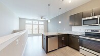 This thoughtfully designed studio offers an efficient and modern living space spread across a single floor. The open-concept layout seamlessly connects the kitchen and living area, creating a cohesive and functional environment.

The kitchen is a standout feature, showcasing dark espresso cabinetry paired with granite-style countertops and a classic white tile backsplash. A peninsula with an undermount sink and integrated dishwasher provides additional prep space and separates the kitchen from the living area. Stainless steel appliances — including a refrigerator, range, and over-the-range microwave — complete the modern culinary setup. Stylish pendant lighting illuminates the workspace, while track lighting adds further ambiance.

The living area is bright and airy, benefiting from large windows that invite generous natural light. A ceiling fan adds comfort and a functional touch to the open space. Light wood-style flooring runs throughout, lending warmth and continuity to the entire unit. A low partition wall defines the transition between the kitchen and living zones, contributing to the open yet organized feel.

The bathroom is clean and well-appointed, featuring a granite-top vanity with dark cabinetry, a large mirror, and a full tub-shower combination, all finished in a neutral, contemporary palette consistent with the rest of the space.