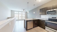 This thoughtfully designed studio offers an efficient and modern living space spread across a single floor. The open-concept layout seamlessly connects the kitchen and living area, creating a cohesive and functional environment.

The kitchen is a standout feature, showcasing dark espresso cabinetry paired with granite-style countertops and a classic white tile backsplash. A peninsula with an undermount sink and integrated dishwasher provides additional prep space and separates the kitchen from the living area. Stainless steel appliances — including a refrigerator, range, and over-the-range microwave — complete the modern culinary setup. Stylish pendant lighting illuminates the workspace, while track lighting adds further ambiance.

The living area is bright and airy, benefiting from large windows that invite generous natural light. A ceiling fan adds comfort and a functional touch to the open space. Light wood-style flooring runs throughout, lending warmth and continuity to the entire unit. A low partition wall defines the transition between the kitchen and living zones, contributing to the open yet organized feel.

The bathroom is clean and well-appointed, featuring a granite-top vanity with dark cabinetry, a large mirror, and a full tub-shower combination, all finished in a neutral, contemporary palette consistent with the rest of the space.