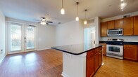 This single-story residence offers a well-designed open-concept layout that seamlessly connects the kitchen and living areas. The kitchen is a functional centerpiece, showcasing rich wood cabinetry extending to the ceiling, dark granite countertops, and a central island with pendant lighting overhead. Stainless steel appliances, including a range, microwave, refrigerator, and dishwasher, complement the space, while hardwood-style flooring runs throughout the main living areas. The living room benefits from natural light through a glass double-door entry and a ceiling fan, creating a bright, airy atmosphere.

The bedrooms feature plush carpeting, ceiling fans, and multiple windows fitted with blinds, allowing ample natural light. The primary bathroom is particularly spacious, offering an elongated granite-topped vanity with warm wood cabinetry, tile flooring, a soaking tub, and direct access to a walk-in closet with built-in shelving. A second full bathroom mirrors the quality finishes with a granite vanity and tile flooring, accompanied by convenient built-in shelving nearby. Overall, the unit presents a cohesive, comfortable design with consistent warm-toned finishes throughout.