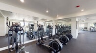 Located at 6400 SW Canyon Ct in Portland, Oregon, this single-floor fitness center is a comprehensively outfitted facility designed to support a wide range of workout routines. The space is organized into several distinct functional zones, each thoughtfully appointed with specialized equipment and finishes.

The cardio area houses a row of SportsArt treadmills alongside multiple elliptical trainers, all positioned adjacent to large windows that bring in natural light and offer views of surrounding greenery. Full-length mirror panels line the walls, visually expanding the space and allowing users to monitor their form during exercise. Recessed lighting throughout maintains a bright, clean atmosphere.

A dedicated cycling studio features a row of stationary spin bikes arranged beneath a wall of windows, creating an open, light-filled environment ideal for group or individual cycling sessions. A projector mounted to the ceiling suggests the room is equipped for instructor-led classes.

The free weights area is stocked with a comprehensive dumbbell rack, stability balls, medicine balls, and a functional training station. Mirrors and windows frame this zone as well, reinforcing the facility's consistent design language. Dark rubber flooring throughout provides both durability and cushioning across all areas of the fitness center.