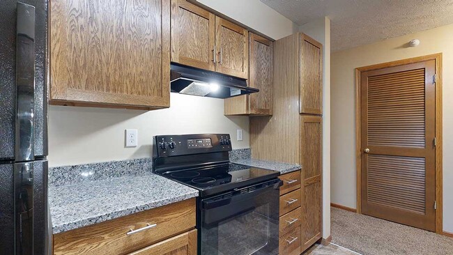 A renovated kitchen in the 1-bedroom Imperial with wooden cabinets, granite countertops, and sleek black appliances. - Pine Lake Heights Apartments