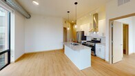 Located at 110 N First St in Minneapolis's North Loop neighborhood, this modern single-floor unit showcases a thoughtfully designed open-concept layout with clean, contemporary finishes. The kitchen serves as the heart of the space, centered around a large island with a quartz countertop, undermount sink, and globe pendant lighting. White shaker cabinetry, a subway tile backsplash, stainless steel appliances including a gas range with a sleek hood vent, and a full-size refrigerator complete the well-appointed cooking area. Exposed ductwork adds an industrial touch that complements the light hardwood flooring found throughout. The living area is bathed in natural light through expansive floor-to-ceiling windows and glass doors that frame sweeping city and skyline views, with a ceiling fan adding comfort. Additional bedrooms also benefit from large windows with outdoor views, enhancing the airy feel of each room. A spacious walk-in closet with built-in wire shelving provides generous storage. The bathroom features a dual-sink vanity with quartz countertops, a large mirror, and a tiled tub-shower combination, alongside a separate glass-enclosed shower. The overall ambiance is bright, clean, and modern throughout.