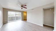 This single-story space offers a clean, functional layout with consistent finishes throughout. The main living areas feature light wood-style flooring that enhances the bright, open feel of the space. A ceiling fan with integrated lighting is centrally positioned overhead, complemented by a textured ceiling. Large sliding glass doors lead to an outdoor balcony, allowing natural light to fill the room and providing exterior views of surrounding greenery.

The kitchen is equipped with stainless steel appliances, including an electric range and an over-the-range microwave. White cabinetry pairs with dark granite-style countertops, creating a classic contrast. Adjacent living and dining areas flow naturally from the kitchen corridor.

The bedrooms are finished with neutral-toned carpet, ceiling fans, and windows that bring in natural light. The rooms maintain a straightforward, versatile layout suitable for a variety of uses. An additional carpeted room, visible in the floor plan, appears to include in-unit laundry.

The bathroom features a full tub and shower combination with floor-to-ceiling tile in a warm gray wood-grain pattern, adding a polished, contemporary touch. Overall, the space presents a cohesive, practical design with updated finishes throughout.