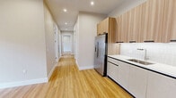 Located at 58 Hamilton Avenue in Passaic, NJ, this thoughtfully updated 3-bedroom, 2-bathroom unit offers a clean, modern aesthetic throughout its single-floor layout. Light wood laminate flooring flows continuously across every room, complemented by crisp white walls, recessed lighting, and bright white baseboards that give the space a fresh, cohesive feel.

The open kitchen and living/dining area serve as the heart of the home. The kitchen is outfitted with two-tone cabinetry — warm wood-grain upper cabinets paired with white lower cabinets — stainless steel appliances including a refrigerator, gas range, and microwave, and a classic white tile backsplash. The adjoining living and dining area benefits from natural light and direct access to the entry door.

A long hallway connects the three bedrooms, each featuring windows with outdoor views, individual wall-unit HVAC systems, and recessed lighting. The generously sized primary bedroom offers ample space and closet access. Additional closets throughout provide plentiful storage, including one walk-in closet with built-in shelving and hanging rods.

Both bathrooms are stylishly appointed with geometric patterned tile flooring, full tub-shower combos with glass enclosures, modern floating vanities, and backlit mirrors. A dedicated laundry area adds everyday convenience to this well-appointed home.