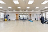 Located at 515 Dunlop Blvd SW in Madison, Alabama, this dedicated fitness center offers a generously sized, single-floor exercise space designed to support a comprehensive workout experience. The open-concept layout provides ample room for movement and accommodates a wide variety of equipment without feeling cramped.

The space is brightly lit by an array of recessed panel ceiling lights complemented by multiple ceiling fans that ensure comfortable airflow throughout. Large windows along the perimeter walls invite abundant natural light while offering views of the surrounding neighborhood, creating an energizing atmosphere. A set of double glass doors provides convenient access and further enhances the sense of openness.

The polished concrete flooring is both durable and easy to maintain, well-suited for high-traffic fitness use. A full-length wall mirror in the strength training area enhances spatial perception and supports proper form during workouts.

Equipment is thoughtfully distributed throughout the room and includes treadmills, elliptical machines, stationary and Peloton cycling bikes, a cable machine system, a power rack with weight plates, a dumbbell rack with a full range of free weights, and a rowing machine. A yoga mat and stability ball round out the functional fitness offerings. The combination of cardio, strength, and flexibility equipment makes this a well-rounded facility suited for diverse fitness routines.