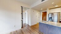 Located in the heart of downtown Jacksonville, this single-floor unit at 112 W Adams St seamlessly merges historic character with contemporary design. The most striking architectural feature is the original exposed red brick walls, which appear prominently in the living area and bedroom spaces, adding warmth and industrial charm to the otherwise clean, modern interior.

The open kitchen is outfitted with granite countertops, dark wood cabinetry, white upper cabinets, a tile backsplash, and stainless steel appliances including an electric range and over-the-range microwave. A kitchen island with a stainless steel sink serves as a functional centerpiece and natural divider between the kitchen and living areas.

The living and sleeping areas feature light hardwood-style flooring and are bathed in natural light through large black-framed windows fitted with horizontal blinds, offering views of the surrounding downtown cityscape. Exposed brick columns frame the windows, reinforcing the building's historic bones.

The bathroom is finished in a clean, all-white palette with large-format floor tiles, subway-tiled tub surround, and a full tub-shower combo with brushed nickel fixtures. The bedroom includes a generously sized closet with wire shelving. Black-framed sliding barn-style doors add a modern industrial accent throughout the unit.