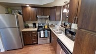 This renovated, corporate-furnished two-bedroom, one-bathroom residence offers a comfortable and functional single-floor layout designed for convenient living. The living room serves as the heart of the home, featuring plush carpeting, a large picture window that invites abundant natural light and outdoor views, and thoughtfully arranged furnishings including a full sofa set, accent chair, and a substantial wood armoire — ideal for media storage. Adjacent to the living room, the dining area accommodates a full six-person table, making it well-suited for both everyday meals and entertaining guests, with a seamless visual connection to the living space. The renovated kitchen is a standout feature, boasting rich dark-wood cabinetry, light granite countertops, hardwood-style flooring, and stainless steel appliances including a range, dishwasher, and refrigerator. Pendant and recessed lighting brighten the workspace, creating a practical and polished culinary environment. Neutral tones, warm textures, and consistent finishes throughout the residence contribute to a cohesive and welcoming ambiance. Fully furnished and move-in ready, this space is ideally suited for corporate or extended-stay occupants seeking a well-appointed, turnkey home.