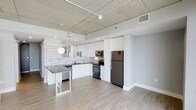 This well-appointed 2-bedroom, 2-bathroom residence offers a thoughtfully designed single-level layout that maximizes both functionality and style. The open-concept floor plan creates a seamless flow between the living and kitchen areas, making the space feel expansive and welcoming.

The kitchen is a standout feature, outfitted with crisp white cabinetry, a subway tile backsplash, and dark countertops that provide striking contrast. Stainless steel appliances — including a full-size refrigerator, built-in microwave, and range — deliver a modern, functional cooking environment. A peninsula with a dark countertop offers additional prep space and serves as a casual dining or entertaining area, complete with a contemporary pendant light above.

Durable light-toned hardwood-style flooring runs throughout the main living areas, adding warmth while complementing the unit's clean aesthetic. The exposed concrete ceiling lends an industrial character to the space, enhanced by track lighting that provides flexible illumination across the open layout.

With two full bathrooms and two bedrooms, this residence is well-suited for a variety of living arrangements. The neutral color palette and modern finishes create a versatile backdrop that adapts effortlessly to a range of interior styles.