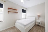 Located at 1831-1835 Harmon St in Berkeley, CA, this private bedroom offers a clean, minimalist design optimized for comfortable, efficient living. The room features light-toned walls paired with light wood-style flooring, creating a bright and airy atmosphere throughout.

A window fitted with a blackout roller shade and a sheer privacy panel allows for flexible light control while maintaining a sense of openness. The ceiling fan overhead provides year-round climate comfort and contributes to the room's clean, functional aesthetic.

Open wooden wall shelves with warm-toned wood brackets add a practical yet stylish storage solution without consuming floor space. A frosted glass sliding closet door provides additional storage while lending a modern, semi-transparent visual element that reflects light and enhances the sense of space.

The entry features a keypad smart lock on the door, offering convenient and secure access. Wall-mounted HVAC vents ensure climate control throughout the space.

Overall, the room presents a thoughtfully arranged, well-lit, and neatly finished interior with a neutral color palette that creates a calm, inviting environment. Its location in Berkeley places it within easy reach of local amenities, the University of California Berkeley campus, and the wider East Bay area.