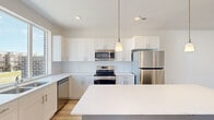 This four-story home offers a thoughtfully organized layout across its multiple levels, providing well-defined living areas suited for a variety of needs. The ground floor houses an attached garage with a concrete floor and direct interior access through a bright, clean entryway finished with light hardwood-style flooring and white walls.

The main living level is the most expansive floor, featuring the kitchen as a central highlight. The kitchen is outfitted with white shaker-style cabinetry, white quartz countertops, a subway tile backsplash, and stainless steel appliances including a range, microwave, and dishwasher. A large picture window floods the space with natural light and provides views of the surrounding neighborhood. An island adds additional counter space and functionality. Light hardwood-style flooring extends throughout this level.

The upper floors accommodate four carpeted bedrooms, including a primary bedroom of comfortable proportions, along with four clean, simply appointed bathrooms featuring white vanities and tile flooring. Multiple staircases connect the levels, supported by hallways that maintain efficient circulation throughout.

The uppermost floor opens to a rooftop terrace, offering open sky views and outdoor space. The home's clean, neutral palette and modern finishes create a cohesive and functional living environment throughout.