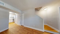 Located at 311 Winston St in Richmond, Virginia, this two-floor home presents a clean, well-maintained interior defined by warm hardwood flooring and neutral gray-toned walls throughout. The main level opens with a welcoming entryway featuring a classic six-panel front door and a window fitted with blinds that allows natural light to fill the space. The open layout connects the main living area directly to the kitchen, creating a functional flow between rooms.

The kitchen is equipped with stainless steel appliances, including a gas range and a full-size refrigerator, complemented by white cabinetry and granite-style countertops that give the space a modern, polished appearance. A staircase leads to the upper floor, where additional rooms continue the consistent hardwood flooring and neutral color palette. Each room on the upper level features windows with blinds, providing natural light and ventilation.

Throughout the home, white baseboards and trim offer a crisp contrast to the warm wood floors, contributing to a cohesive and tidy aesthetic. The layout, as revealed by a three-dimensional overview, is compact yet efficiently arranged, making practical use of the available space across both floors.