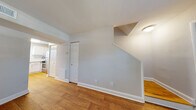 Located at 311 Winston St in Richmond, Virginia, this two-floor home presents a clean, well-maintained interior defined by warm hardwood flooring and neutral gray-toned walls throughout. The main level opens with a welcoming entryway featuring a classic six-panel front door and a window fitted with blinds that allows natural light to fill the space. The open layout connects the main living area directly to the kitchen, creating a functional flow between rooms.

The kitchen is equipped with stainless steel appliances, including a gas range and a full-size refrigerator, complemented by white cabinetry and granite-style countertops that give the space a modern, polished appearance. A staircase leads to the upper floor, where additional rooms continue the consistent hardwood flooring and neutral color palette. Each room on the upper level features windows with blinds, providing natural light and ventilation.

Throughout the home, white baseboards and trim offer a crisp contrast to the warm wood floors, contributing to a cohesive and tidy aesthetic. The layout, as revealed by a three-dimensional overview, is compact yet efficiently arranged, making practical use of the available space across both floors.
