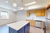 Located at 8 S Sixth St in Council Bluffs, Iowa, this one-bedroom, one-bathroom unit offers a well-organized layout across a single floor. The kitchen serves as a standout feature, showcasing warm wood cabinetry, white subway tile backsplash, a white quartz countertop, and a striking navy blue island with pendant globe lighting overhead. Stainless steel appliances—including a refrigerator, dishwasher, range, and microwave—complete the functional and stylish cooking space. The layout flows through a bright, carpeted hallway lined with recessed lighting and clean white walls, connecting the main living areas to the private spaces. The bedroom is a comfortable, well-proportioned room with soft carpet flooring, neutral walls, and a dedicated closet with double doors, providing ample storage. An additional closet space is also accessible off the hallway. The bathroom features a full tub-shower combo, a wood-tone vanity with white countertop, single sink, and a large mirror, maintaining the cohesive, clean aesthetic found throughout the unit. The overall ambiance is fresh, modern, and move-in ready, with a consistent neutral palette accented by warm wood tones and bold design choices in the kitchen.