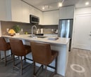 Located at Unit 112 on 104th Ave in Surrey, BC, this thoughtfully designed 400 sq ft, one-bedroom, one-bathroom ground-floor unit offers a modern and efficient living space. The open-concept layout seamlessly connects the kitchen and living room, maximizing the use of every square foot.

The kitchen is a standout feature, boasting flat-panel white cabinetry extending to the ceiling, a grey tile backsplash, quartz countertops, and a full suite of stainless steel appliances including a range, over-the-range microwave, dishwasher, and refrigerator. A peninsula with bar seating provides additional prep space and casual dining.

The living room is bright and welcoming, with large windows and a glass door that invite natural light and offer outdoor views. Light-toned laminate flooring runs throughout the main living areas, contributing to the unit's airy, contemporary feel.

The bedroom, at 80 sq ft, is a cozy and practical retreat featuring a window with outdoor views and carpeted flooring. The bathroom is finished with a wood-toned vanity, quartz countertop, undermount sink, and large mirror, complemented by neutral tile flooring. A connecting hallway provides a smooth transition between all rooms, completing this well-appointed urban unit.