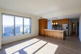 Located in the heart of downtown Los Angeles, this modern high-rise residence at 225 S Grand Ave offers a sophisticated urban living experience with sweeping panoramic views of the city skyline. The open-concept layout is thoughtfully designed with clean lines and contemporary finishes throughout.

The kitchen is a standout feature, outfitted with warm wood cabinetry, stainless steel appliances including a built-in microwave and range, light quartz countertops, a mosaic tile backsplash, and polished tile flooring. A large window frames impressive city views, flooding the space with natural light.

The living and bedroom areas showcase wide-plank hardwood flooring and plush carpeting, respectively, with expansive floor-to-ceiling windows that capture breathtaking views of the Los Angeles skyline and surrounding cityscape. Generous closet space and clean white walls provide a versatile, move-in-ready canvas.

The primary bathroom features dual sinks set in a rich wood vanity topped with marble-style countertops, large-format gray tile surrounding a soaking tub and glass-enclosed shower, and recessed lighting. A secondary bathroom mirrors the same refined aesthetic with a single vanity and tub-shower combination. The overall ambiance is bright, minimal, and polished.