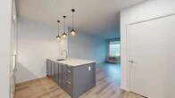 Located at 55 Riverside Dr in Yonkers, NY, this thoughtfully designed one-bedroom, one-bathroom residence offers a refined modern aesthetic throughout. Light wood-tone flooring runs seamlessly across the open-plan layout, complementing the clean white walls and contemporary finishes.

The kitchen is a standout feature, showcasing two-tone cabinetry — crisp white upper cabinets paired with slate-blue lower cabinetry — topped with marble-style quartz countertops. A central island with an undermount sink and brushed nickel faucet provides additional prep space and casual seating potential. Striking globe pendant lights in warm gold tones add an elegant finishing touch. The kitchen is equipped with a gas range and built-in oven.

The open living area flows naturally from the kitchen, benefiting from large windows and direct balcony access through full glass doors, offering views of the landscaped courtyard and the Hudson River beyond. The private balcony features glass railings, enhancing the connection to outdoor scenery.

The bedroom is a well-proportioned retreat with large windows that invite natural light and frame outdoor views. Three closets, including generously sized walk-in storage, offer practical organization.

The bathroom is finished with marble-look tile flooring, a white vanity with quartz countertop and brass fixtures, and a sleek walk-in shower, creating a clean, spa-like atmosphere.