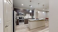 This single-story, one-bedroom, one-bathroom unit offers a well-designed open-concept layout that efficiently utilizes its space. Light wood-style flooring runs continuously throughout, complementing the neutral beige tones on the walls and creating a cohesive, modern aesthetic.

The combined kitchen and living area serves as the centerpiece of the unit. The kitchen is outfitted with dark espresso-toned cabinetry, a white subway tile backsplash, stainless steel appliances including a refrigerator, range, and built-in microwave, and a granite-topped island with pendant lighting above. The island provides additional counter space and functions as a breakfast bar. Recessed lighting and ceiling fans are found throughout, adding both practicality and style.

The living area flows seamlessly from the kitchen and features a private entry door with adjacent windows that bring in natural light. The bedroom is a comfortable, well-proportioned room with a ceiling fan, a window with blinds, and access to a walk-in closet.

The bathroom includes a dark wood vanity with a granite countertop, a large mirror with overhead lighting, a glass-enclosed tiled shower, and continued wood-style flooring, maintaining consistency with the rest of the unit.