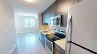 Located at 2827 Telek Place in Alexandria, Virginia, this one-bedroom, one-bathroom residence offers a thoughtfully organized single-level layout. The kitchen is a standout feature, outfitted with dark wood cabinetry, stainless steel appliances including a range, microwave, and refrigerator, a tile backsplash, and a white countertop with an undermount sink. Light wood-tone flooring runs through the kitchen and hallway, creating a clean, contemporary feel that connects the main areas of the home. The bedroom is a comfortable retreat, carpeted in warm neutral tones and featuring a sliding double-panel closet and a window with blinds that frames outdoor greenery, allowing natural light to fill the room. The bathroom is finished with large-format light tile flooring, a dark wood vanity with an undermount sink, a wall-mounted mirror, and recessed lighting, maintaining the modern aesthetic carried throughout the space. Neutral gray walls with crisp white trim unify the home's interior palette, giving the space a clean and cohesive look. The layout makes efficient use of space, with a practical flow from the entry hallway through to the kitchen, bathroom, and bedroom. This residence offers a modern, move-in-ready environment in a desirable Alexandria location.