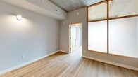 Located at 127 N 17th St in Richmond, Virginia, this single-floor unit offers a thoughtfully designed open-concept layout that maximizes its compact footprint. Light hardwood flooring runs throughout, creating a warm and cohesive aesthetic that ties the living and kitchen areas together seamlessly.

The kitchen is a standout feature, showcasing white shaker cabinetry, granite countertops, a subway tile backsplash, and stainless steel appliances including a range with a wall-mounted hood vent. A peninsula with an undermount sink and pendant lighting above adds both functionality and style, making it an inviting space for cooking and casual dining.

The living area benefits from large windows with warm wood-toned frames that allow natural light to filter in, complementing the exposed concrete ceiling — an industrial architectural detail that adds character and visual interest to the space.

The bathroom is finished with a clean, modern aesthetic, featuring a full soaking tub and tub surround clad in crisp white subway tile, paired with sleek chrome fixtures for a polished look.

Overall, this unit blends contemporary finishes with industrial design elements, resulting in a stylish and functional space well-suited to urban living in Richmond's historic district.