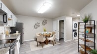 This single-floor residence offers a thoughtfully designed layout encompassing two bedrooms, three bathrooms, a dedicated office, and a combined living, dining, and kitchen area. Light wood-style flooring flows consistently throughout, complemented by neutral warm-gray walls that lend a clean and cohesive aesthetic.

The kitchen features crisp white shaker cabinetry, granite countertops, a classic subway tile backsplash, and a full suite of stainless steel appliances. It opens directly into the dining area, where a round wooden table is situated beneath a flush ceiling light fixture. A stacked in-unit washer and dryer is conveniently located nearby, alongside built-in closet storage.

The living room benefits from a large window dressed with sheer white curtains, allowing ample natural light to fill the space. The primary bedroom includes a window with blinds and dedicated wardrobe storage. The second bedroom also features a window and open closet space, while the office provides a bright, functional area with its own window.

The three bathrooms are finished with wood-look flooring and shower-tub combinations with curtain enclosures. A connecting hallway ties the private areas of the residence together efficiently. Overall, the space delivers a modern, comfortable, and practical living environment.